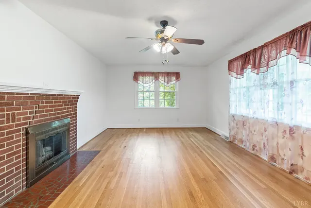 an empty room with wooden floor fireplace and windows