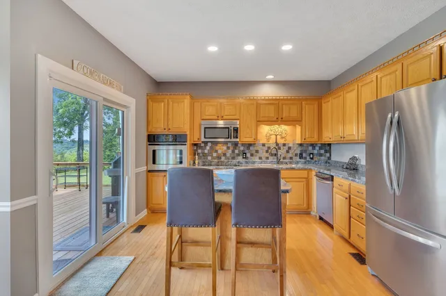 a kitchen with stainless steel appliances granite countertop a refrigerator a stove top oven and a dining table with wooden floor