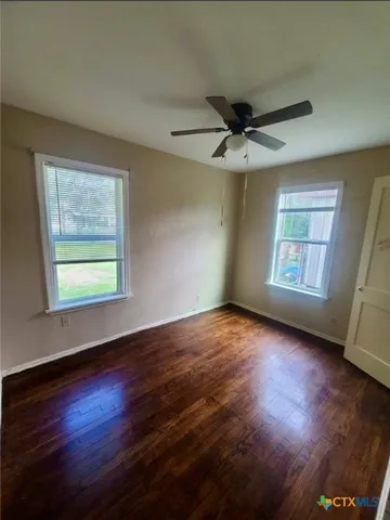an empty room with wooden floor chandelier fan and windows