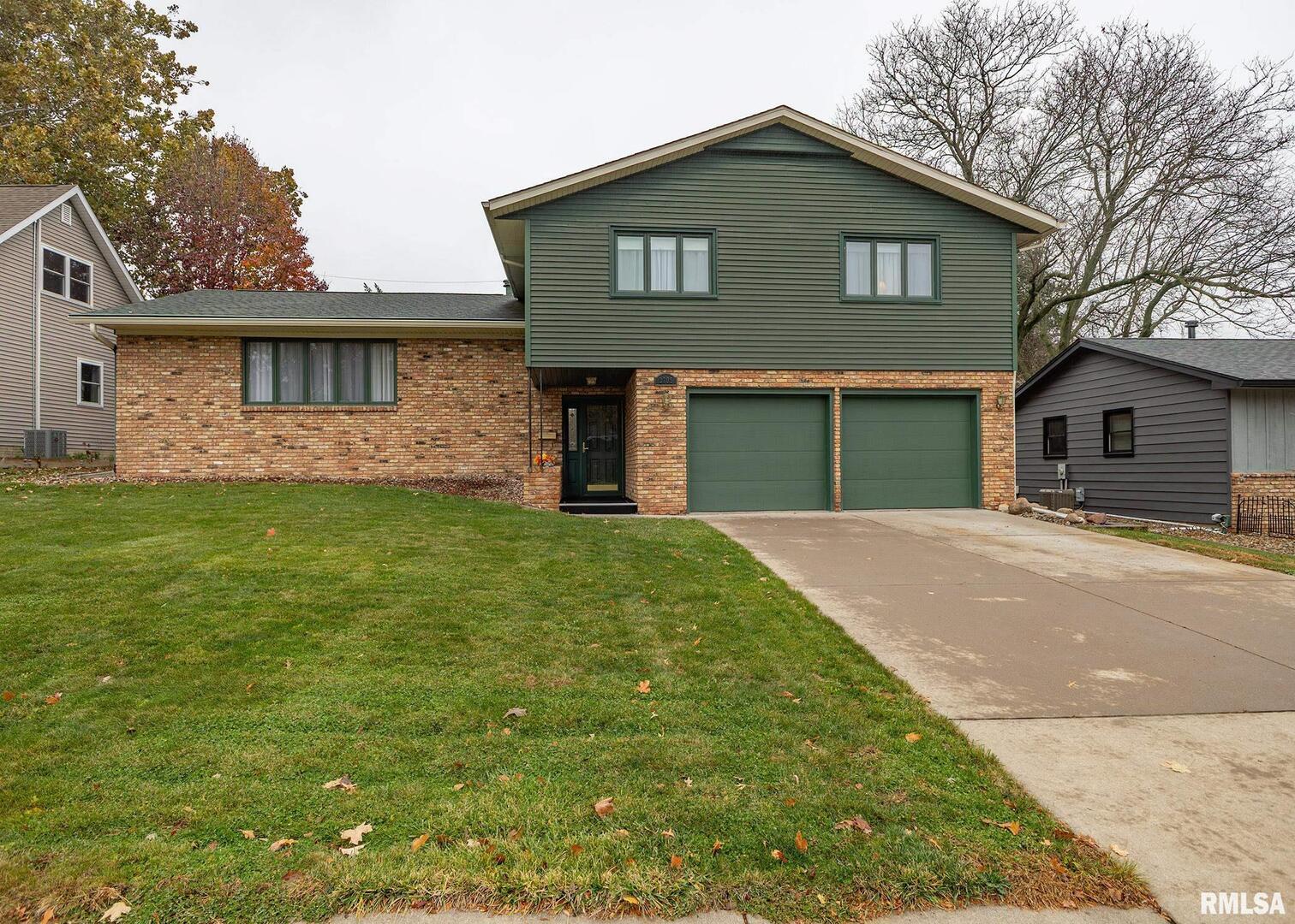 a house that is sitting in the grass with large windows and a large tree