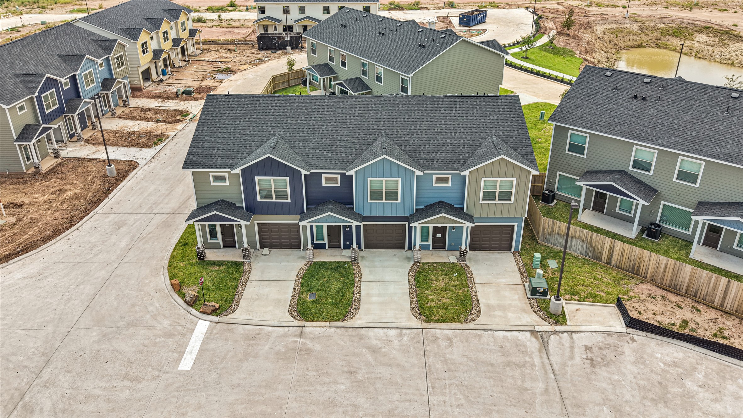 14010 Longstreet Road, Unit 2 Willis, TX 77318 - Photo 3 of 29 This photo shows a modern townhouse complex with multiple units, each featuring a garage and small front yard. The homes have a contemporary design with varied siding colors. The neighborhood is newly developed, with paved roads and surrounding green spaces.