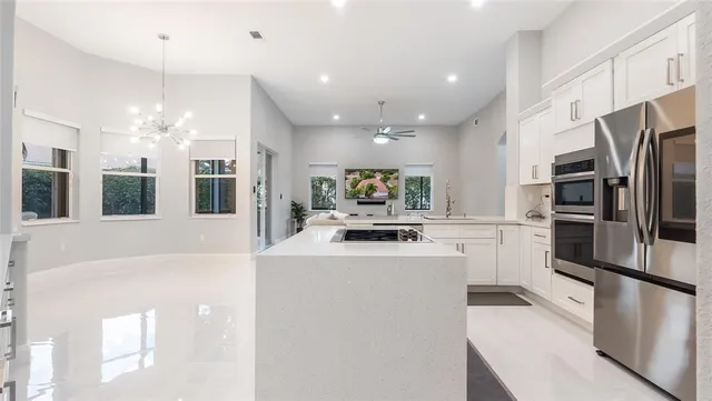 a kitchen with stainless steel appliances kitchen island granite countertop a refrigerator oven a sink dishwasher and white cabinets with wooden floor