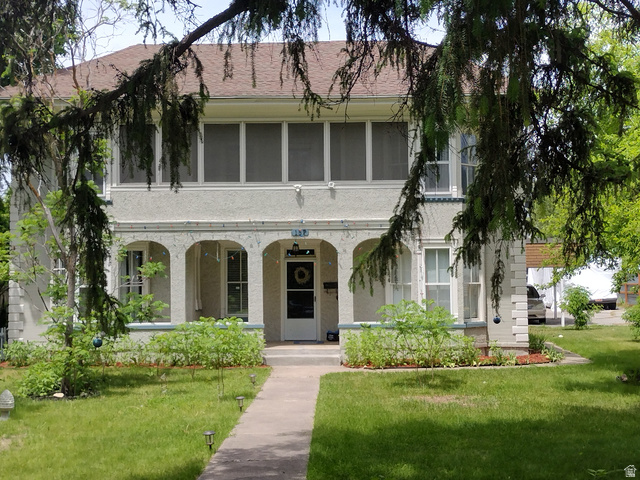 Two-story stucco residence featuring an arched portico, upper-level enclosed porch, a gabled roof, and a front walkway
