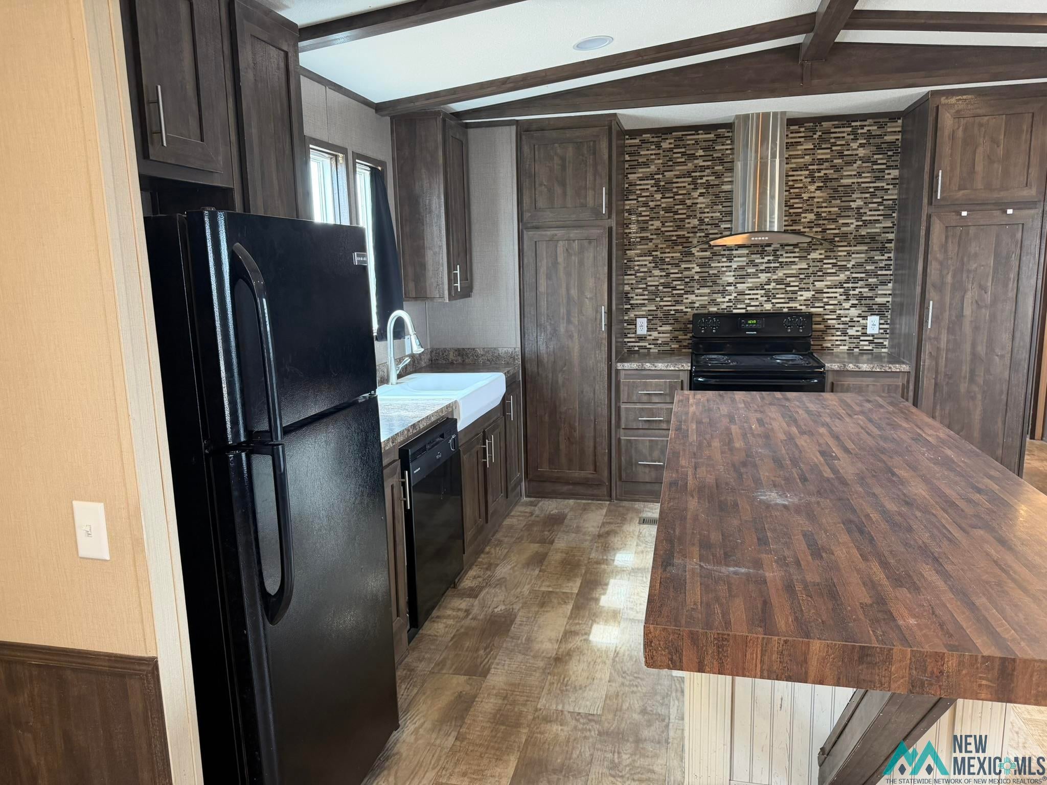 801 Riata Road Carlsbad, NM 88220 - Photo 6 of 39 Kitchen featuring wood-finish flooring, dark wood cabinetry, a tiled backsplash, a farmhouse sink, and a large wood-finish island