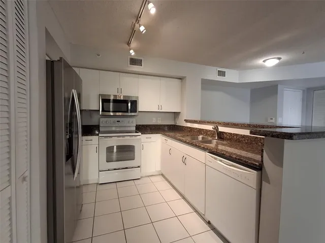a white kitchen with granite countertop a stove top oven microwave and refrigerator