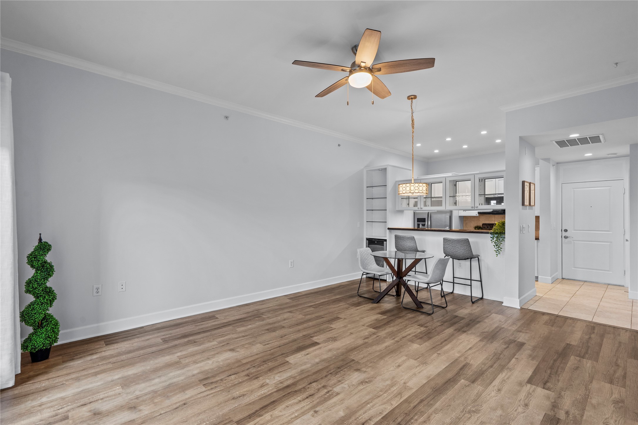 1900 Genesee Street, Unit 203 Houston, TX 77006 - Photo 5 of 30 This photo showcases a bright, open-concept living area with wood flooring and neutral walls. It features a ceiling fan, modern light fixtures, and an integrated kitchen with a breakfast bar. The space is airy and well-lit, ideal for both relaxation and entertaining.