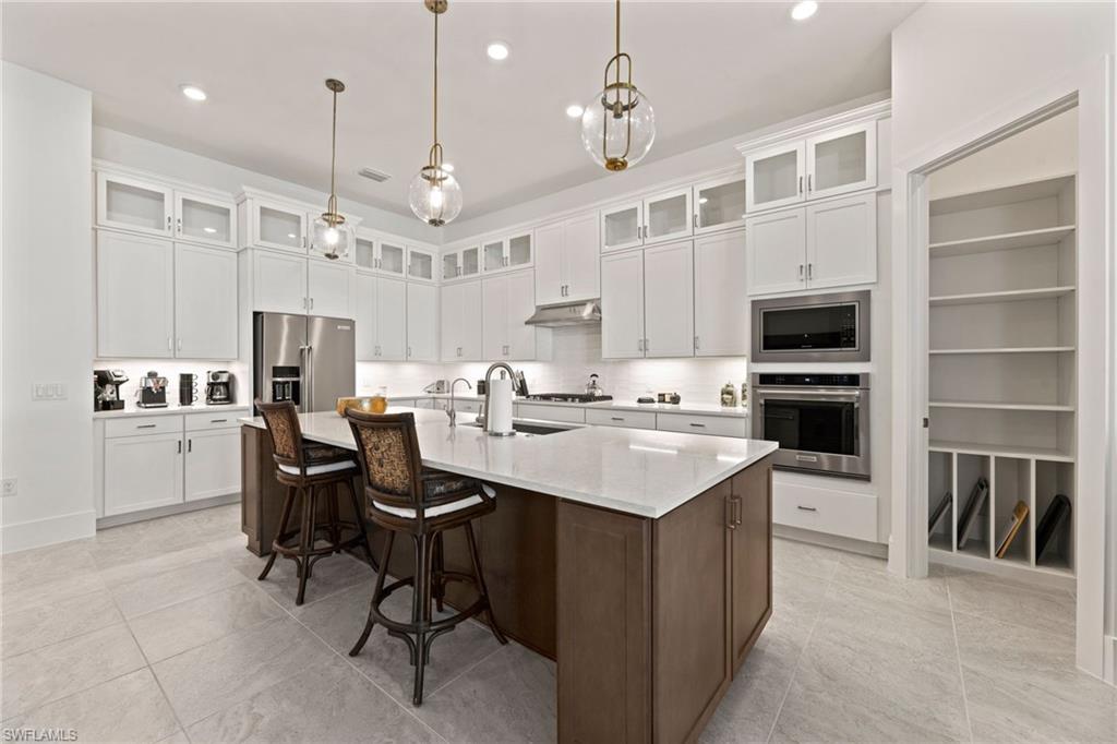 16140 Verilyn Circle Naples, FL 34110 - Photo 9 of 44 a large kitchen with kitchen island a center island a stove a dining table and chairs