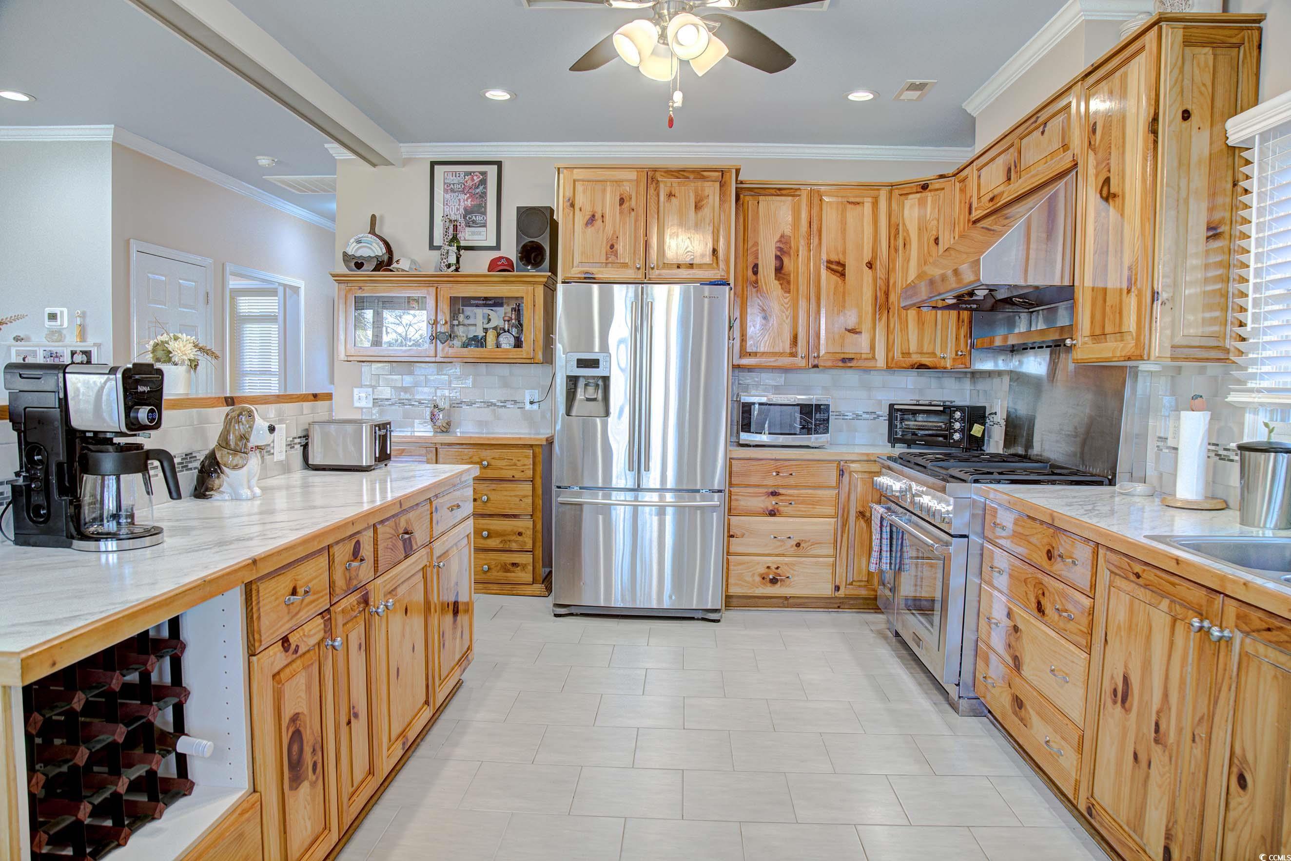 3637 Choppee Road Georgetown, SC 29440 - Photo 15 of 40 Kitchen featuring stainless steel appliances, decorative backsplash, under cabinet range hood, crown molding, and glass insert cabinets
