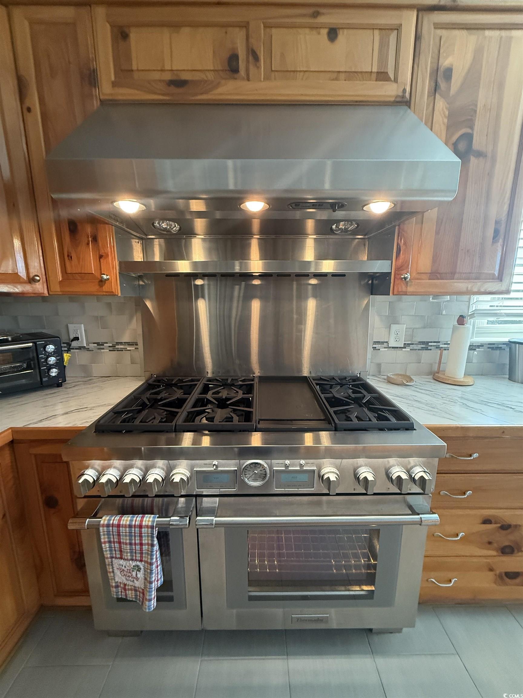 3637 Choppee Road Georgetown, SC 29440 - Photo 16 of 40 Kitchen featuring exhaust hood, light countertops, decorative backsplash, range with two ovens, and brown cabinets