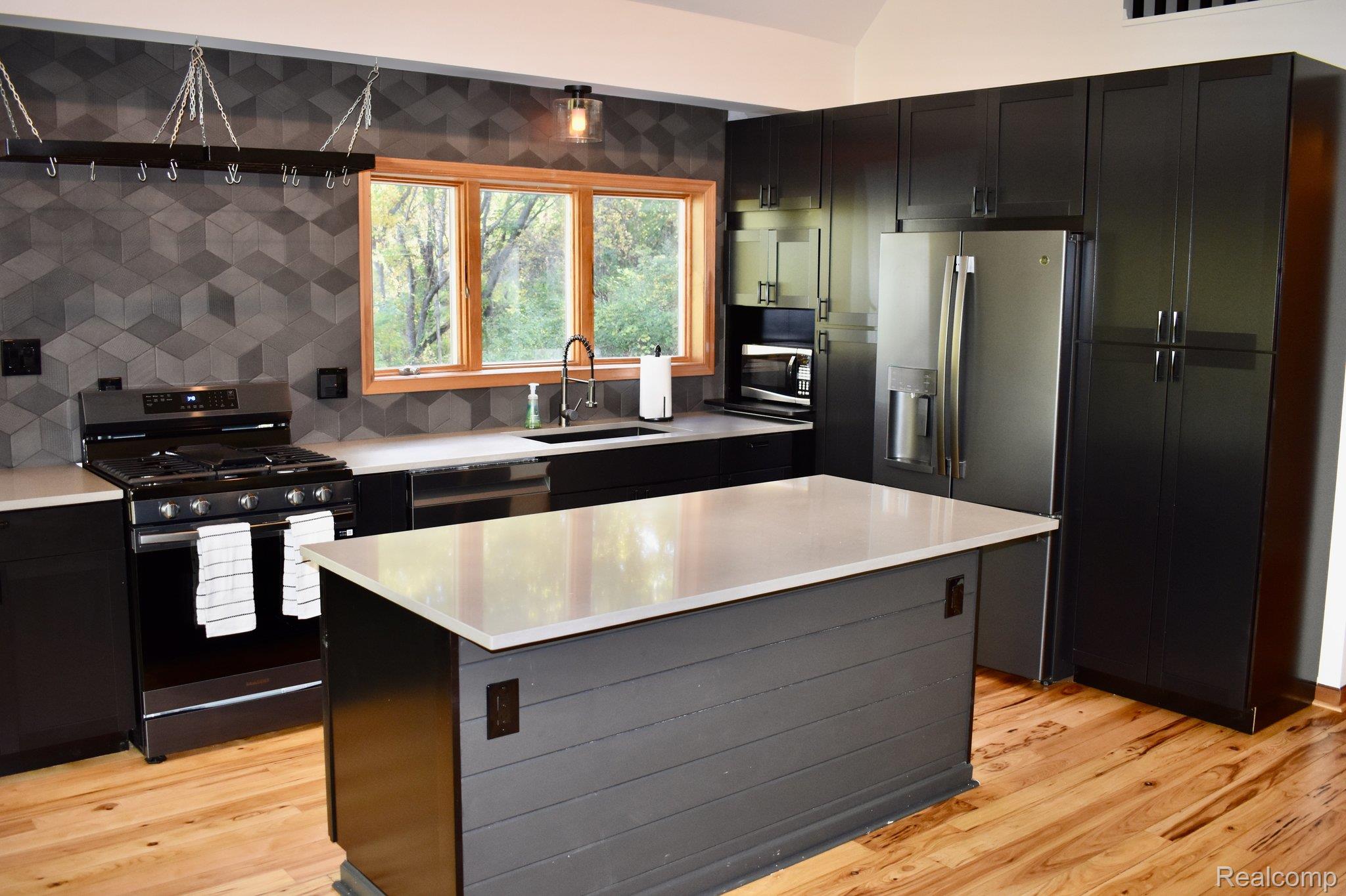 8312 Whitmore Lake Road Brighton, MI 48116 - Photo 27 of 43 Kitchen featuring dark cabinetry, stainless steel appliances, a center island with a light-toned countertop, wood-finish flooring, and a dimensional tile backsplash