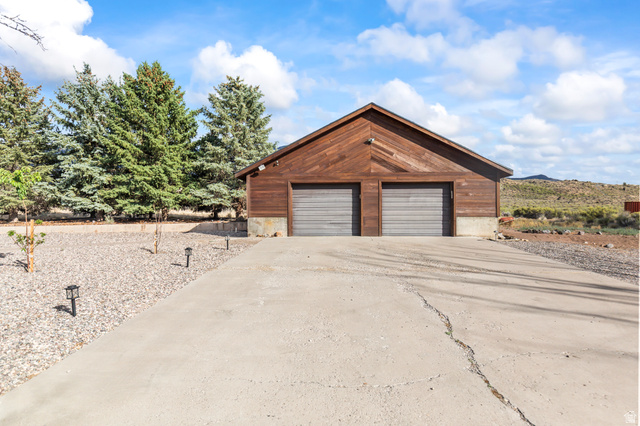 460 Omni Point Road Central Valley, UT 84754 - Photo 81 of 101 Wood-sided garage building featuring two roll-up garage doors, a concrete driveway, and gravel landscaping with mature evergreen trees