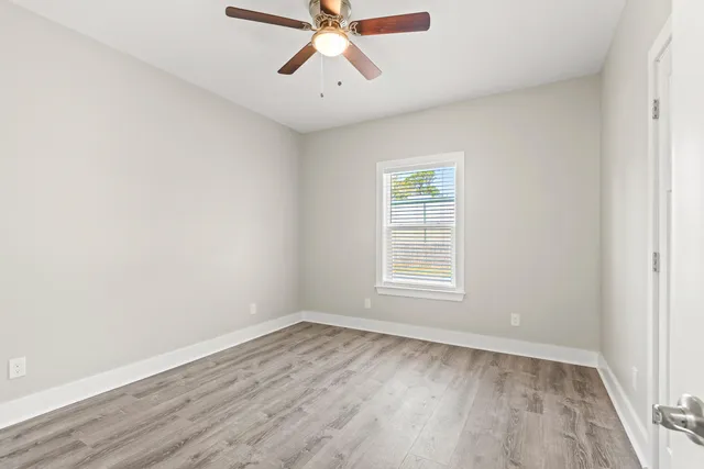 an empty room with wooden floor chandelier fan and windows