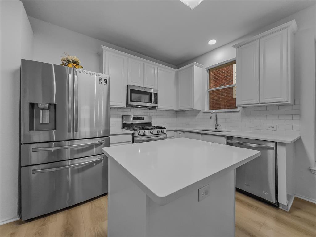 3008 Devlin Ridge Drive Plano, TX 75025 - Photo 5 of 24 Modern kitchen featuring a central island with a solid surface countertop, stainless steel appliances, white shaker-style cabinetry, subway tile backsplash, and light wood-finish flooring