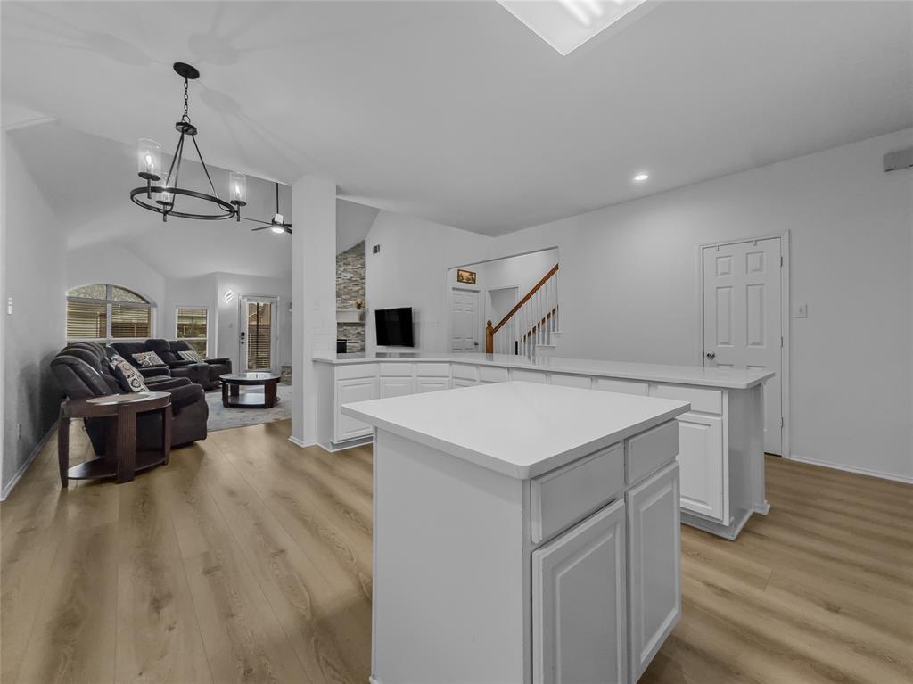 3008 Devlin Ridge Drive Plano, TX 75025 - Photo 8 of 24 Open-concept living space featuring wood-finish flooring, vaulted ceilings, and a kitchen island with white cabinetry and solid surface countertops