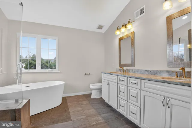 a spacious bathroom with a granite countertop double vanity sink a mirror and a bathtub