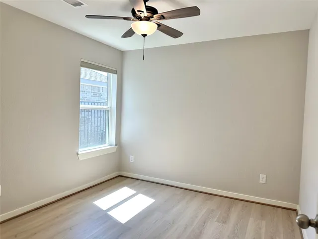 an empty room with wooden floor chandelier fan and windows