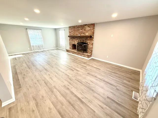 an empty room with wooden floor fireplace and windows