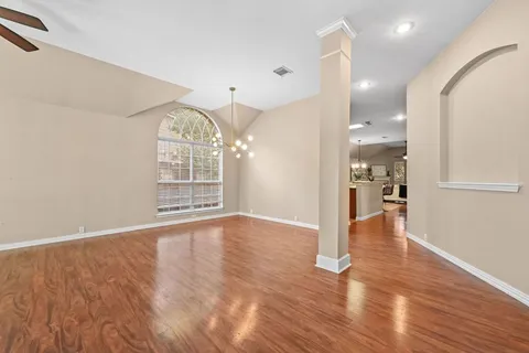 a view of an empty room with wooden floor and a kitchen