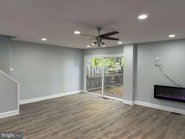 a view of an empty room with wooden floor and a ceiling fan