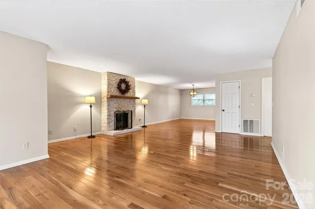 a view of an empty room with wooden floor fireplace and a window