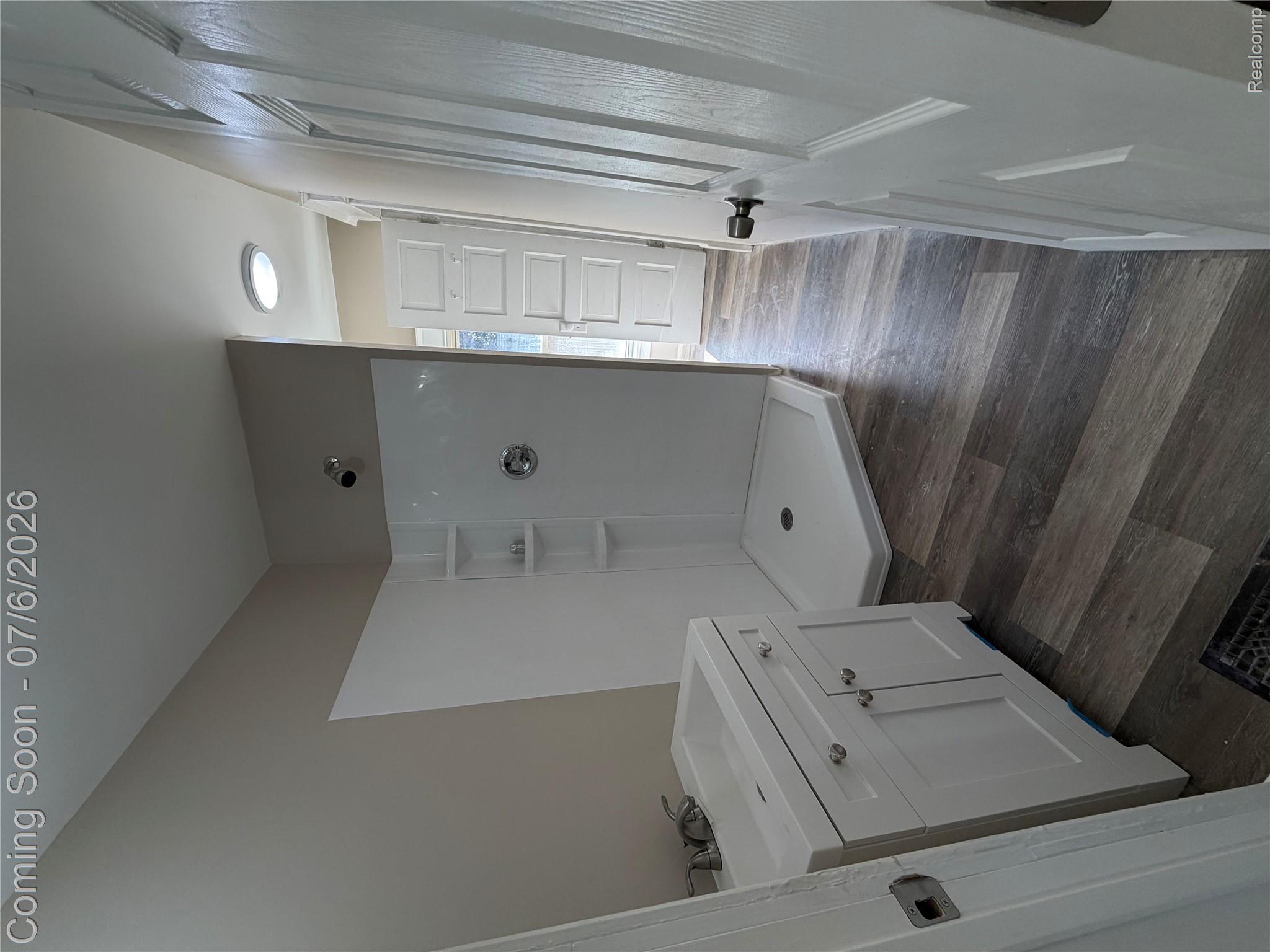 808 Division Street Owosso, MI 48867 - Photo 15 of 25 Compact bathroom featuring a white vanity with integrated sink, a corner shower stall, wood-finish flooring, and light-toned walls