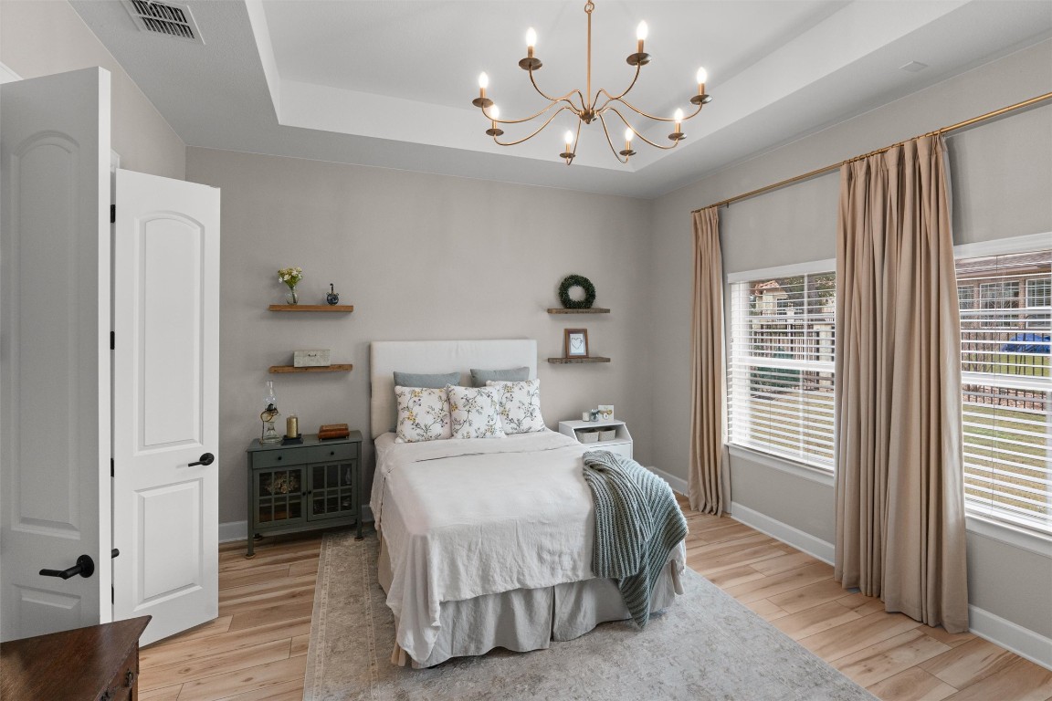 313 Racing Oak Loop San Marcos, TX 78666 - Photo 18 of 39 This is a large primary bedroom with a tray ceiling, chandelier, draperies and floating shelves on each side of the bed.