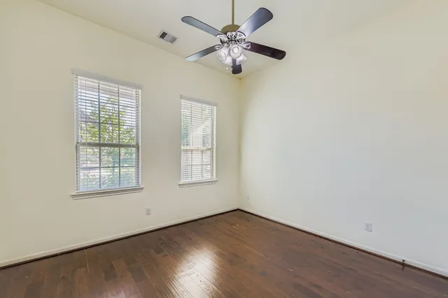 an empty room with wooden floor chandelier fan and windows
