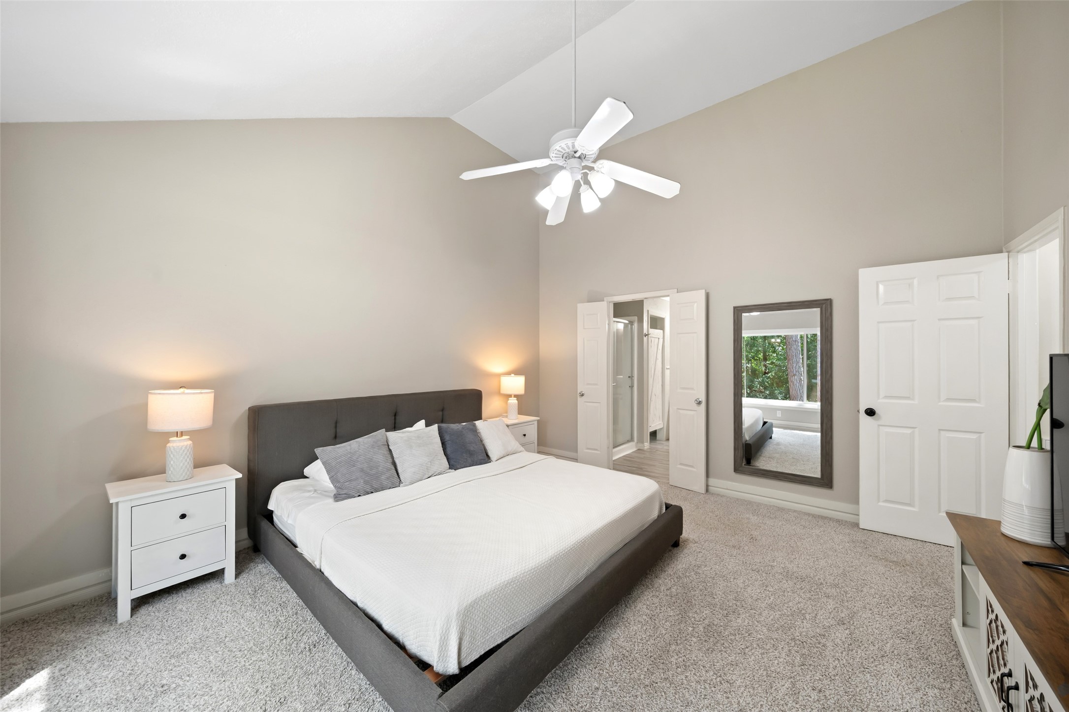 3 East Stony Bridge Circle Spring, TX 77381 - Photo 25 of 42 This primary bedroom features high ceilings, a modern ceiling fan, and large windows that provide abundant natural light and direct views of the garden. The functional layout includes carpeting, a walk-in closet, and direct access to the well-lit en suite bathroom.
