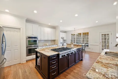 a kitchen with stainless steel appliances granite countertop a stove a sink dishwasher a refrigerator and white cabinets with wooden floor