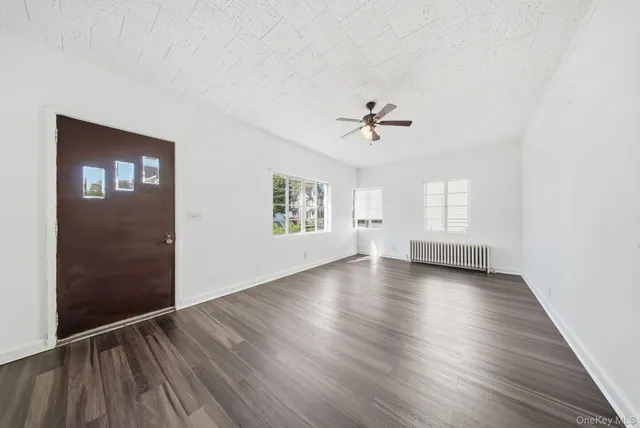 an empty room with wooden floor chandelier fan and windows