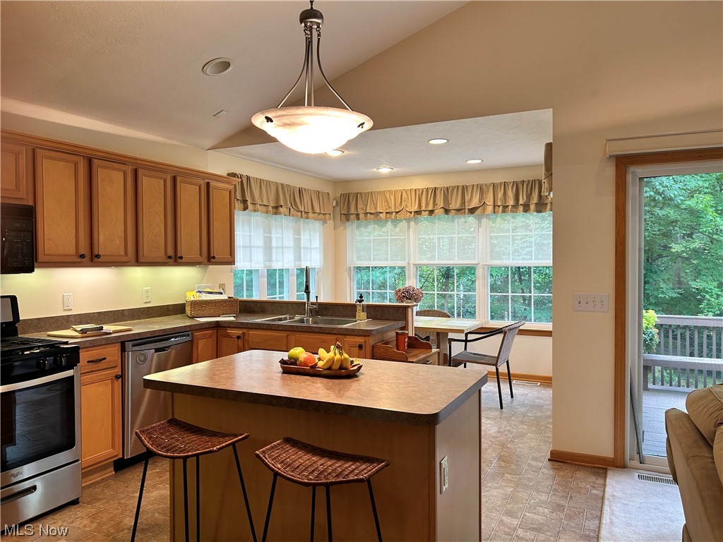 14600 Valentine Road Thompson, OH 44086 - Photo 8 of 31 Kitchen featuring brown cabinets, a kitchen island, appliances with stainless steel finishes, plenty of natural light, and lofted ceiling