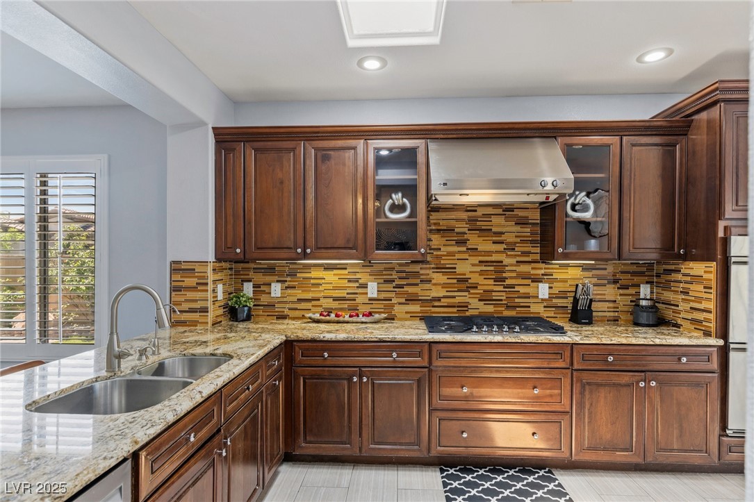 3 Chatmoss Road Henderson, NV 89052 - Photo 9 of 41 Kitchen with a sink, stainless steel gas stovetop, wall chimney exhaust hood, decorative backsplash, and light stone counters
