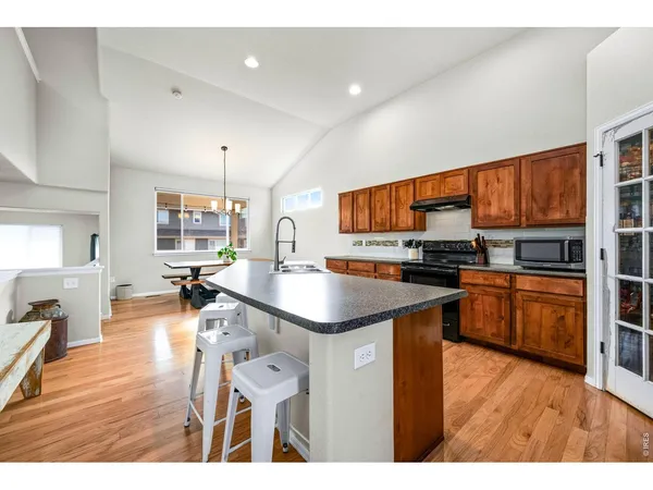 a open kitchen with stainless steel appliances granite countertop a refrigerator a stove top oven a sink dishwasher and wooden cabinets with wooden floor