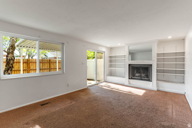 728 400 East Orem, UT 84097 - Photo 12 of 30 Living area featuring a fireplace with a white mantel, built-in shelving, a sliding glass door, and a window overlooking a wooden fence