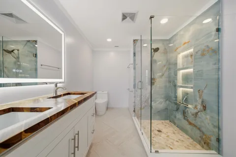 a bathroom with a granite countertop sink a toilet a mirror and shower