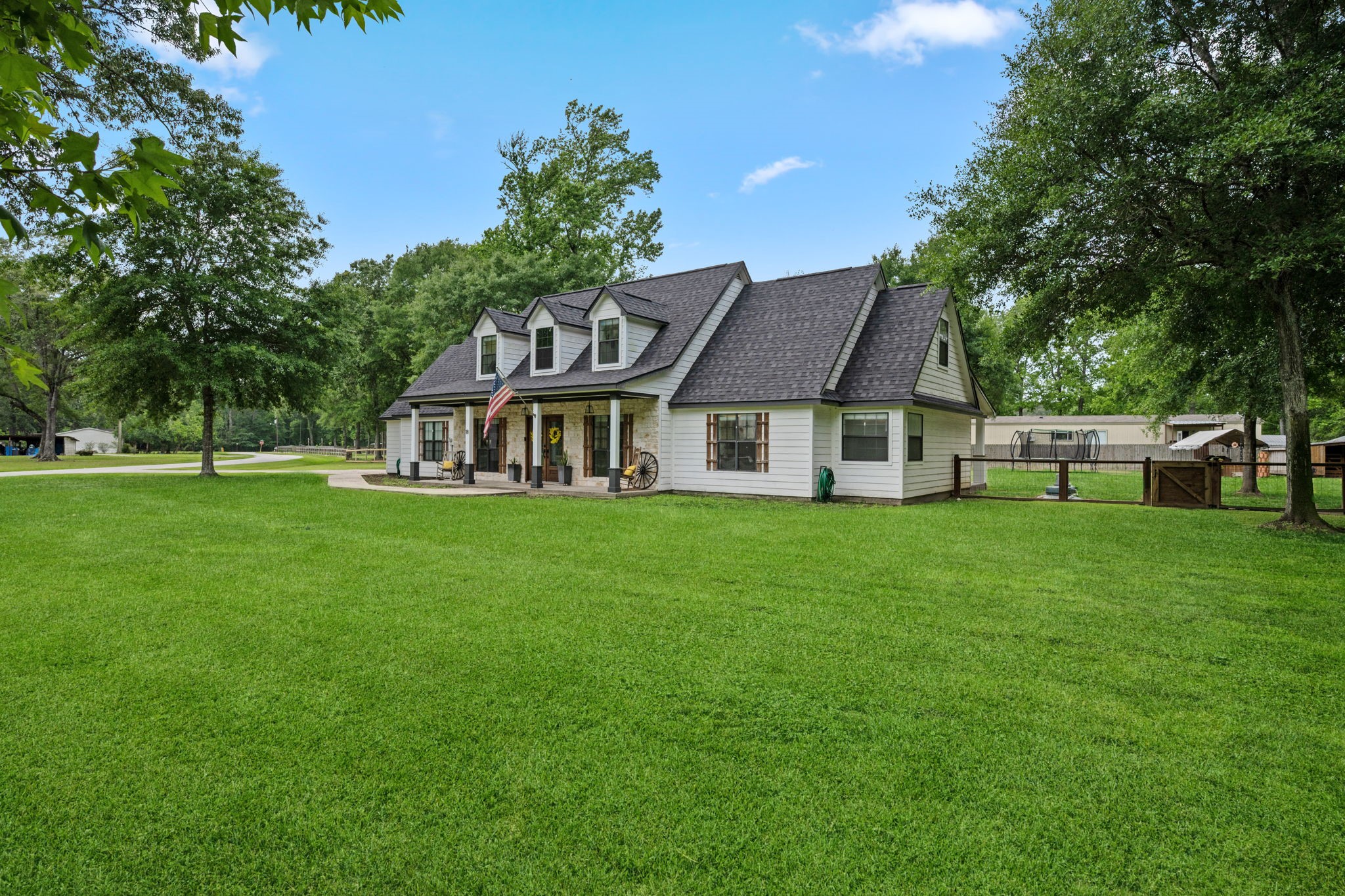 18 East Old Field Road Huffman, TX 77336 - Photo 35 of 35 Stunning side perspective of the home highlighting the charming farmhouse-inspired exterior, oversized lawn, & serene wooded surroundings that complete this exceptional country retreat.