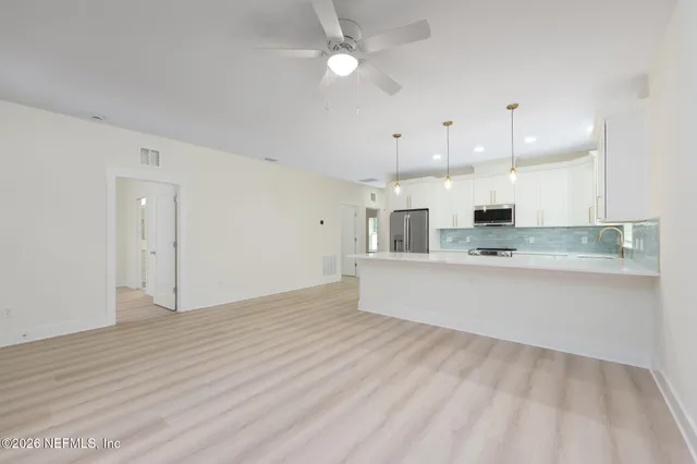 a large kitchen with stainless steel appliances granite countertop a refrigerator a oven and white cabinets with wooden floor