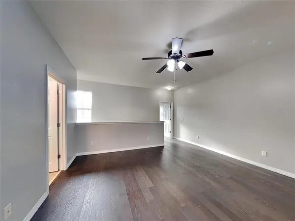 an empty room with wooden floor ceiling fan and windows