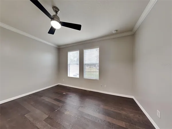 an empty room with wooden floor fan and windows
