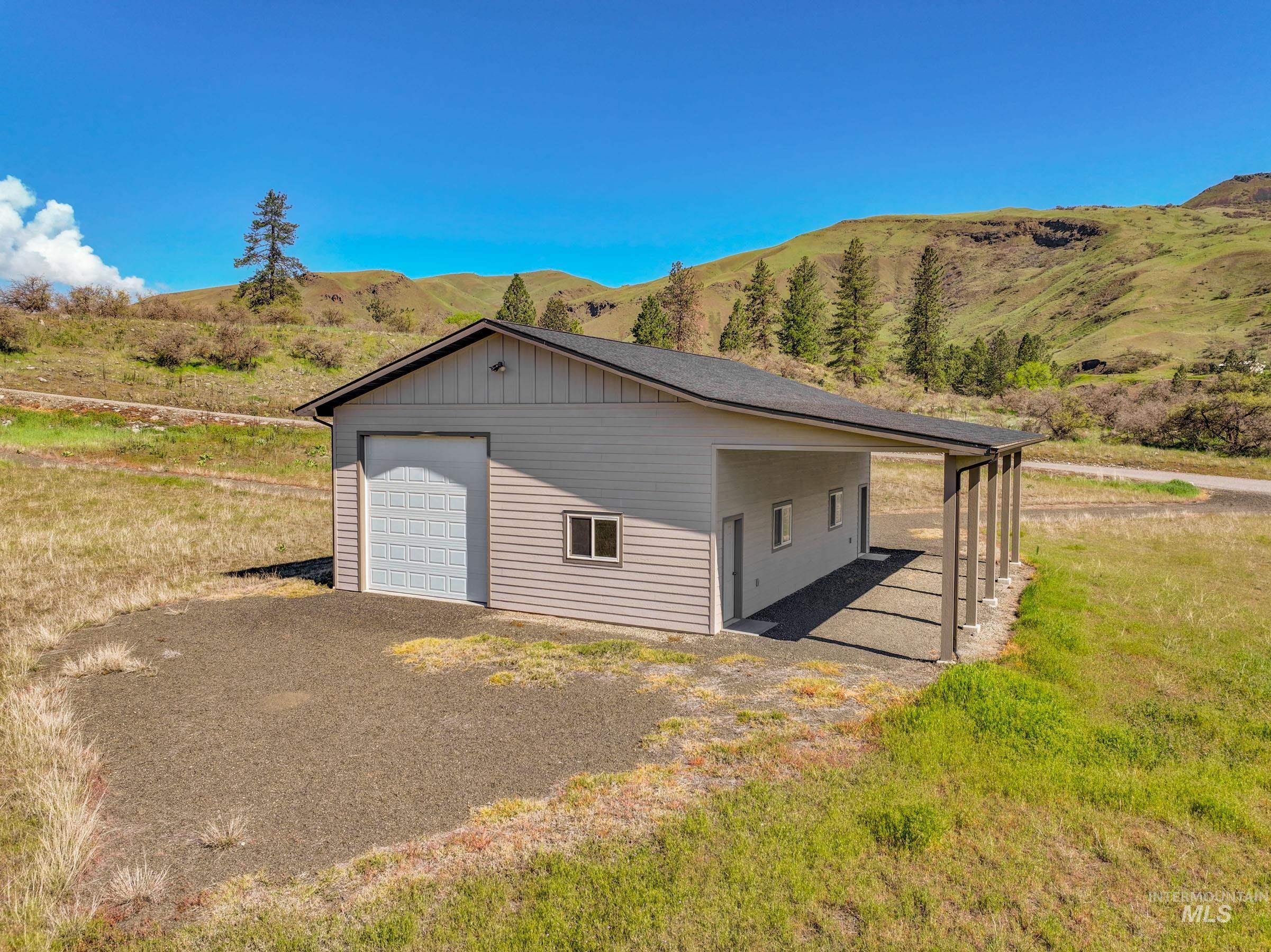 113 Deford Road White Bird, ID 83554 - Photo 46 of 49 Detached structure featuring light gray siding, a single garage door, and a covered carport supported by columns
