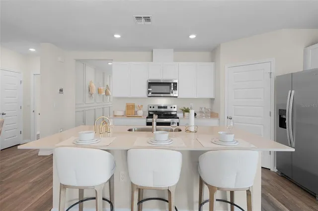 a kitchen with stainless steel appliances granite countertop a dining table chairs refrigerator and sink