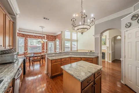a very nice looking kitchen with granite countertop a stove dining table and chairs with wooden floor