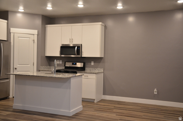 1842 South 1280th Street West Logan, UT 84321 - Photo 4 of 21 Modern kitchen featuring an island with an integrated sink, white cabinetry, speckled countertops, and stainless steel appliances