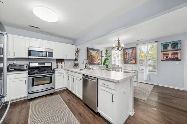 a kitchen with stainless steel appliances granite countertop a stove top oven a sink dishwasher and white cabinets with wooden floor