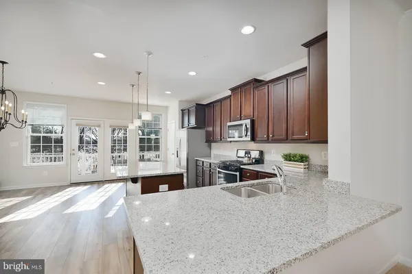 a open kitchen with granite countertop a stove top oven a sink a dining table and chairs with wooden floor