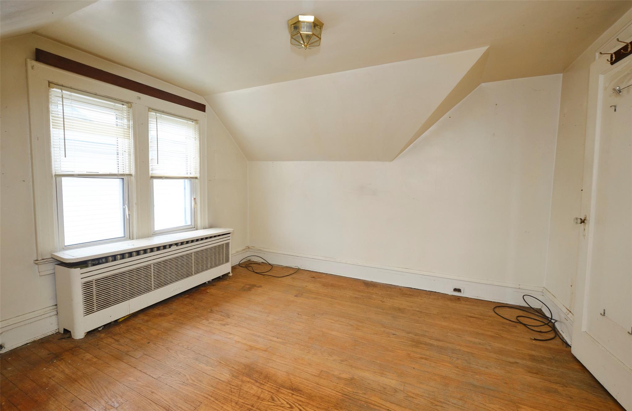 135-47 229th Street Queens, NY 11413 - Photo 21 of 36 Additional living space featuring radiator heating unit, light wood-style flooring, and vaulted ceiling
