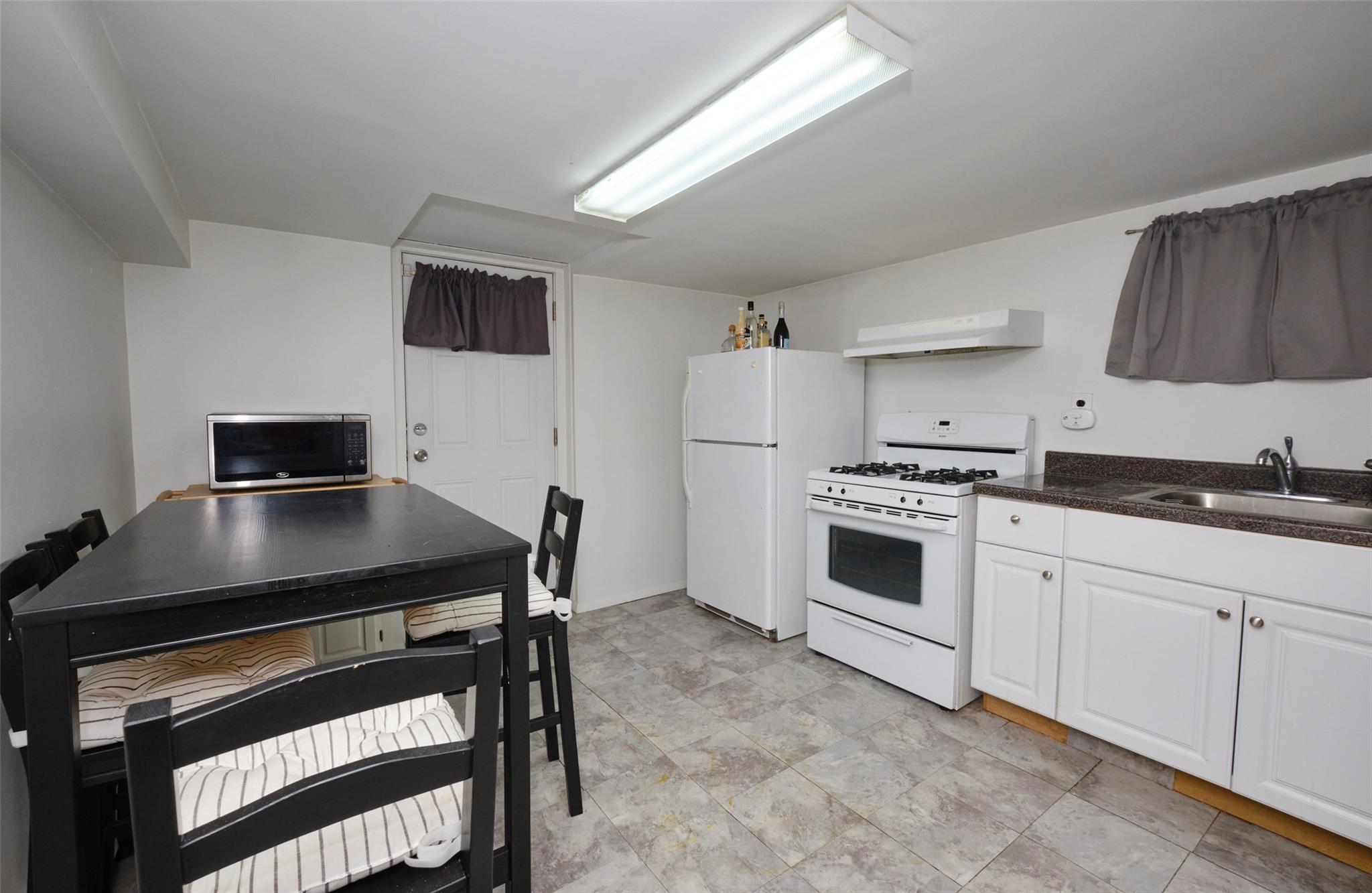 135-47 229th Street Queens, NY 11413 - Photo 26 of 36 Kitchen featuring a sink, white cabinetry, under cabinet range hood, white appliances, and dark countertops