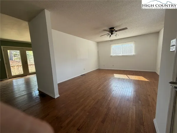 an empty room with wooden floor chandelier and windows