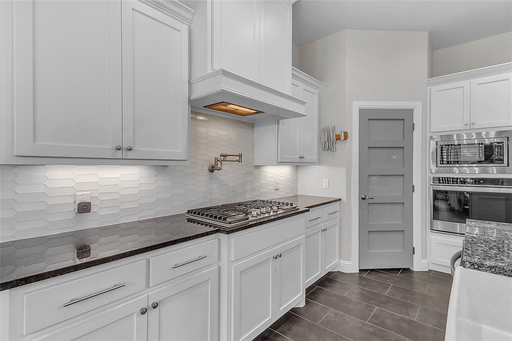 1014 Rennard Street Caddo Mills, TX 75135 - Photo 12 of 39 Kitchen featuring shaker cabinetry, gas range, generous-sized walk-in pantry with paneled door, granite countertops, a gas range with a pot filler faucet, stainless steel built-in appliances, and a gray paneled door