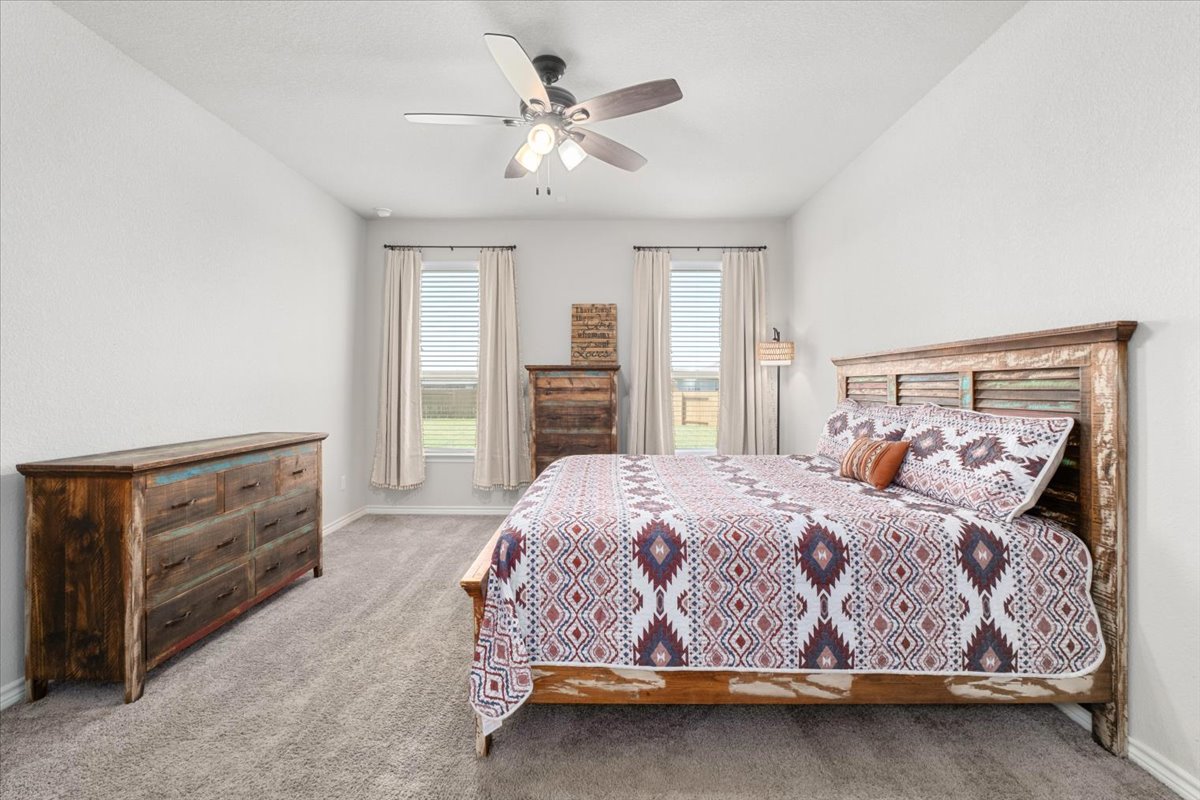 5408 Vanner Path Georgetown, TX 78626 - Photo 17 of 34 Spacious bedroom featuring light neutral wall tones, two large windows with blinds and drapes, and a ceiling fan with integrated lighting